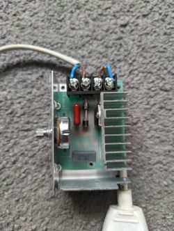 Otwarty regulator elektroniczny z radiatorem, potencjometrem i zaciskami na szarej powierzchni.