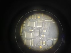 Płyta elektroniczna pod mikroskopem z widocznymi elementami układu scalonego.
