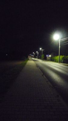 Nocna ulica oświetlona latarniami, wzdłuż której biegnie chodnik z kostki brukowej