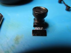 Camera module with lens on blue background Small modular camera placed on a blue surface.