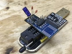 CH341A programmer with SOP16 adapter and capacitors on a wooden surface.