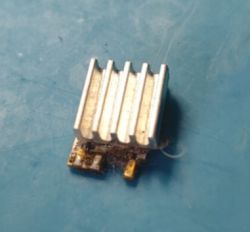 Small electronic module with an aluminum heatsink on a blue work surface.