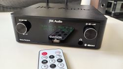 Amplituner JRK Audio Evothon z wyświetlaczem LCD, pokrętłami sterującymi, pilotem oraz portem USB na przednim panelu.