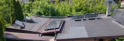 Panele fotowoltaiczne na dachu budynku otoczone zielenią.