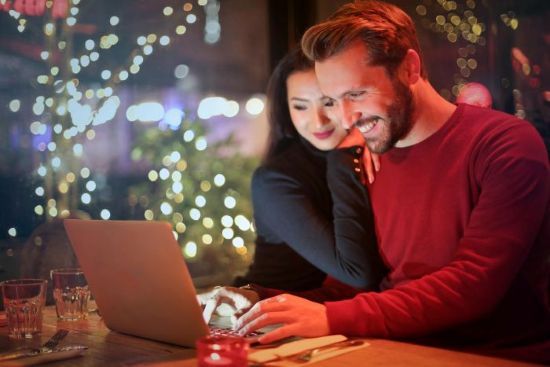Para przy laptopie w restauracji z dekoracjami świątecznymi Para ogląda coś na laptopie w restauracji, otoczona świątecznymi światłami.