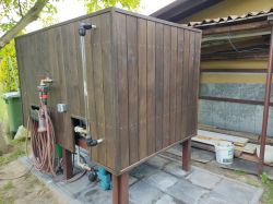 Wooden box with hoses and plumbing elements outside a building.