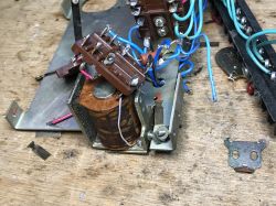 Disassembled relay internals: coil, contact block on brown insulator, and blue wires on a workbench