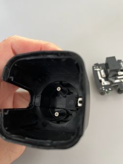 Interior of a plastic casing with two protruding pins and a disassembled electronic component.