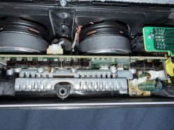 Wnętrze urządzenia elektronicznego z widocznymi kondensatorami i cewką pokrytą brązowo-czarną substancją