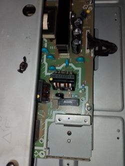 Zbliżenie na płytę zasilającą urządzenia elektronicznego z widocznymi kondensatorami i transformatorem.