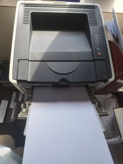 Drukarka laserowa z wysuniętą kartką papieru.