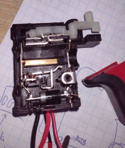 Wnętrze rozłożonego przełącznika z widocznymi elementami elektrycznymi na kartce w kratkę.