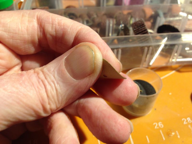 Zbliżenie na rękę trzymającą cienką tarczę szlifierską. W tle widać plastikowe pudełko z akcesoriami.