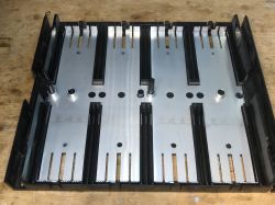 Black plastic chassis with four metal guide plates and module slots, on a wooden surface