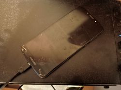 Uszkodzony smartfon Motorola z czarnym ekranem podłączony kablem USB do komputera.