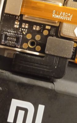 Zbliżenie na wewnętrzne elementy telefonu Xiaomi Mi 11 Lite 5G z widocznymi pinami i taśmą.