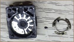 Rozebrany enkoder mechaniczny z widocznymi elementami wewnętrznymi, leżący na stole obok uszkodzonego metalowego pierścienia.