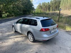 Silver Volkswagen station wagon parked on an unpaved road near a forest.