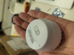 A person holding a white water leak detector with Wi-Fi function in their hand.