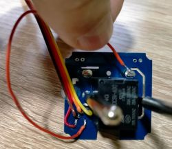 Close-up of a printed circuit board with a relay and colored wires soldered to it.