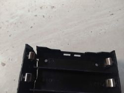 Close-up of a damaged plastic battery holder for cylindrical cells, visible crack on the left side.