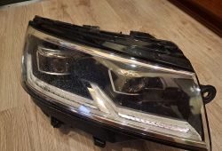 Przednia lampa full LED T6 z numerem 7L1941036A leży na drewnianej podłodze.