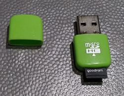 Zielony czytnik kart microSD HC USB z plastikową zatyczką obok, na czarnym fakturowanym tle.