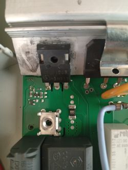 Zbliżenie na tranzystor mocy IGBT przymocowany do radiatora na płytce PCB wraz z innymi elementami elektronicznymi.