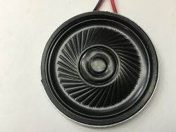 Black round loudspeaker with ribbed cone on a light background, red and black wires at the top