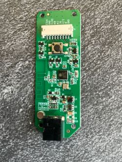 Nahaufnahme einer grünen Leiterplatte mit verschiedenen elektronischen Bauteilen, einschließlich eines Knopfes und eines Steckverbinders.