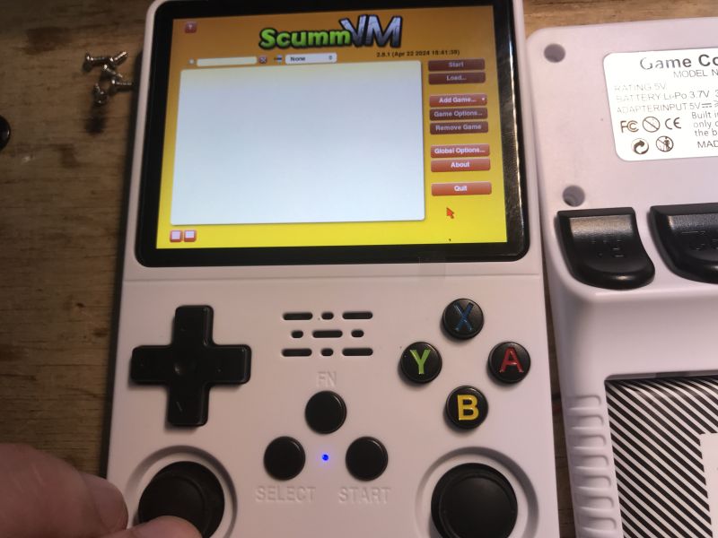 Handheld retro console with ScummVM interface open on screen, placed on wooden surface