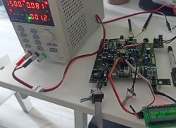 Zdjęcie przedstawia stanowisko testowe z zasilaczem laboratoryjnym oraz prototypową płytką amplitunera z wyświetlaczem LCD.