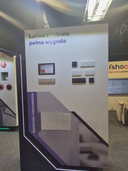 Trade-show display with control panels and switches; text “Łatwa kontrola, pełna wygoda”.