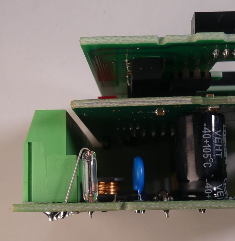 Płytka PCB z elektroniką, widoczny kondensator elektrolityczny, cewka i złącze terminalowe.