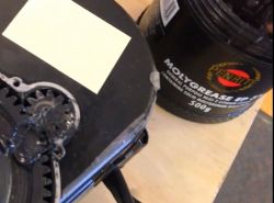 Pojemnik z czarnym smarem obok części mechanicznej.