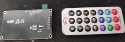 Back of a 2.4 TFT SPI display module with labeled pins, next to a small remote control
