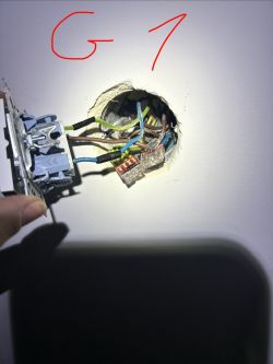 Otwarta puszka w ścianie z przewodami i złączkami, obok trzymany mechanizm łącznika.
