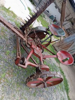 Stara kosiarka mechaniczna z metalowym siedziskiem i malowanymi na czerwono elementami.