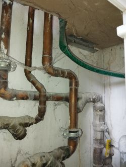 Instalacja rur miedzianych i metalowych pod sufitem z pajęczynami.