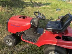 Czerwony traktorek Husqvarna na trawie, widok z boku, z czarnym siedzeniem i kierownicą.
