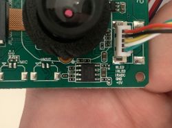 Close-up of a camera module with a lens, PCB board, and a connector with colored wires.