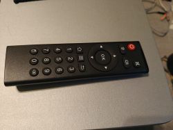 Black remote control with numeric keypad and OK button on a gray surface