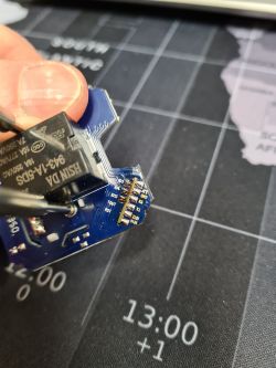 A person holding an ESP-02S module mounted on a PCB, with a multimeter probe touching components.