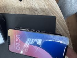 iPhone 13 Pro ze zdeformowanym i częściowo oddzielonym wyświetlaczem leżący na czarnej powierzchni.