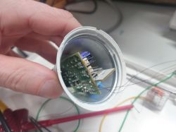 Hand holding an opened electronic device with a visible circuit board and wires.