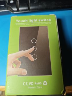 Packaging of a touch light switch in green, featuring an image of a hand touching icons on a panel.