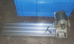 Silnik zamocowany na metalowym profilu z niebieskim pojemnikiem w tle