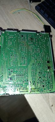 Spód zielonej płytki PCB z licznymi lutami i ścieżkami, leżącej na drewnianym blacie