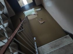 Zalana klatka schodowa z widoczną wodą pokrywającą schody i unoszącymi się przedmiotami.
