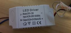 Biały zasilacz LED DF8-12W, z opisem parametrów wejścia i wyjścia, leżący na drewnianej powierzchni.